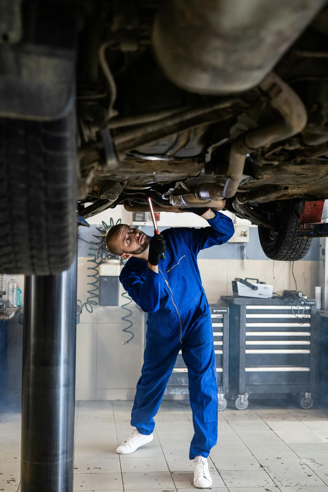 Technicien travaillant sous une voiture levée sur un pont élévateur d'atelier